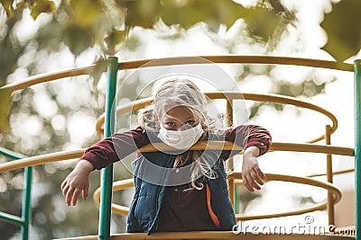 Upset girl wearing a mask on the playground, protecting against a pandemic. Boredom during quarantine, social distance Stock Photo