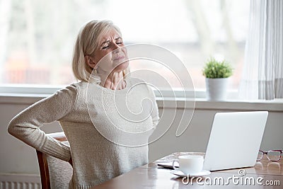 Upset mature woman sitting feeling back pain massaging aching mu Stock Photo