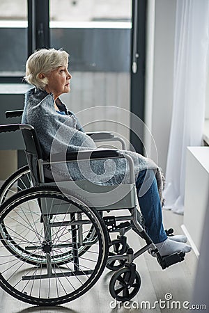 Upset mature woman sitting in wheelchair in room Stock Photo