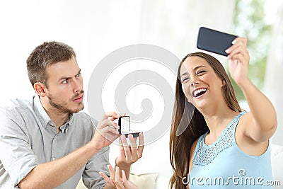 Upset man proposing marriage and girlfriend taking selfie Stock Photo
