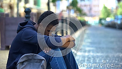 Upset multi-ethnic boy lonely sitting on sidewalk, family conflict, rebellion Stock Photo