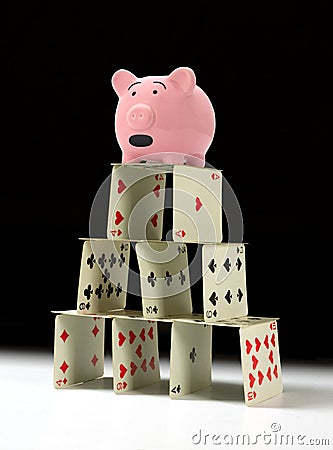 Upset piggy bank standing on fragile shaky house of cards with a dark background Stock Photo