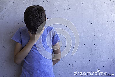 Upset sad boy stand alone and leaning on gray wall. Learning difficulties, family problems, bullying, depression, stress Stock Photo