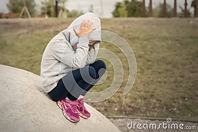 Upset sad depressed little school girl sitting alone at city street park clutching head. Upset stressed frustrated child lost Stock Photo