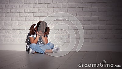 Upset sad sad child girl in stress cries at an empty dark wall Stock Photo