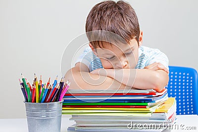 Upset schoolboy sitting at desk with pile of school books and notebooks Stock Photo