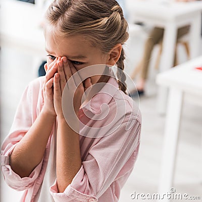 Upset schoolkid near table crying in Stock Photo