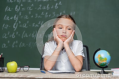 upset schoolkid sitting at desk near Stock Photo