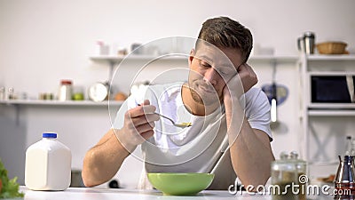 Upset single man eating tasteless cereals for breakfast, lack of appetite Stock Photo