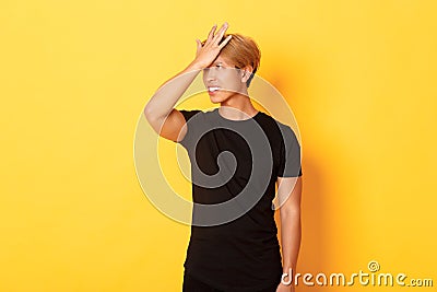 Upset and troubled asian guy snap forehead forgetful, standing over yellow background Stock Photo