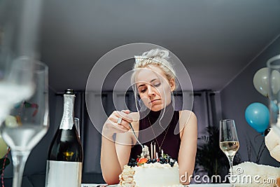 Upset, unhappy attractive woman eating festive cake while celebrating birthday at home, sitting alone at served table Stock Photo