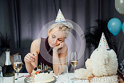 Upset, unhappy attractive woman eating festive cake while celebrating birthday at home, sitting alone at served table looking away Stock Photo