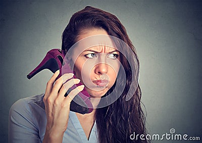 Upset woman holding high heeled shoe in her hand as phone Stock Photo