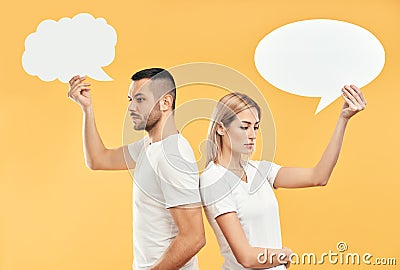 Upset woman and man holding paper thought bubbles over yellow background Stock Photo