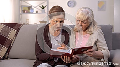 Upset women looking through photo album remembering past times, sad memories Stock Photo