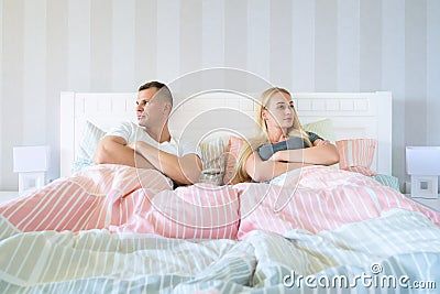 Upset young couple having marital problems or a disagreement sitting side by side in bed facing in opposite directions Stock Photo