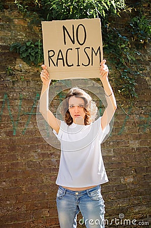 Upset young protesting woman in white shirt holds protest sign broadsheet placard with slogan `No racism` for public Stock Photo