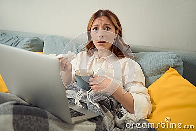Dejected female with notebook computer and cup in bedroom Stock Photo