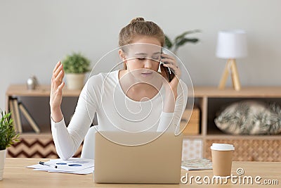 Upset female working ta laptop having unpleasant talk on phone Stock Photo