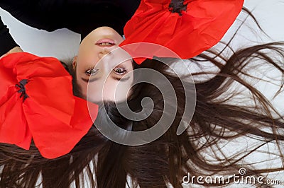 Upside down portrait of beautiful young sexy woman lying on the floor with long wide hair and fashion red paper poppies Stock Photo