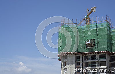 Upward view of precast building cover by green net, large tall Tower Crane moving machine in construction work, under clear blue Stock Photo