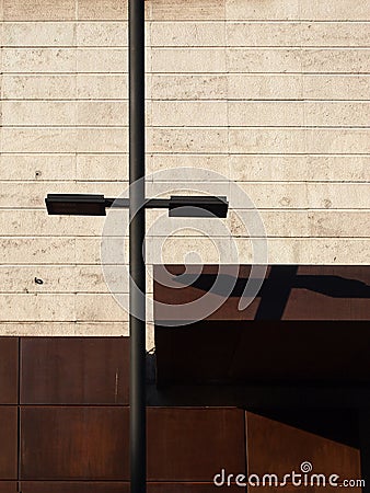 Urban abstract scene with a street lamp casting a shadow shadow on a sunlit wall with stone blocks and rusty steel tiles Stock Photo