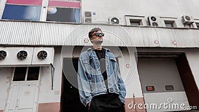Urban cool young hipster man in youth stylish clothes in trendy sunglasses stands near a vintage white building in the city on a Stock Photo