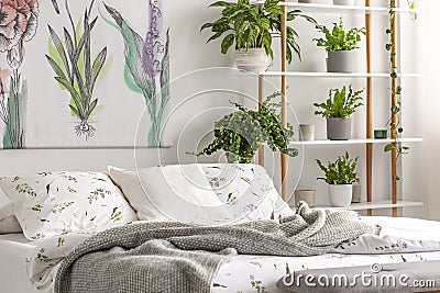 Urban jungle bedroom interior with plants in pots beside a bed dressed in organic cotton linen of white color with green print. Re Stock Photo