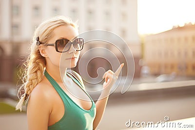 Urban portrait of stylish happy model blonde girl in green dress and sunglasses with hair plaited in a braid posing at Stock Photo