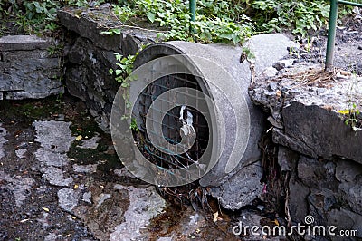 urban river: water oozes out of a round pipe, blocked by an old grate Stock Photo