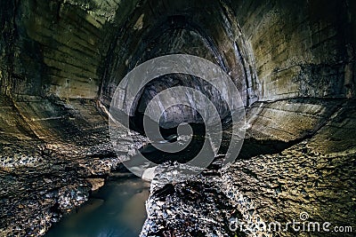 Urban sewage flowing through large oviform underground turning sewer tunnel Stock Photo