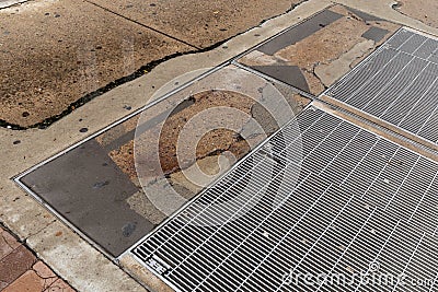 Urban sidewalk with heavy metal grates, cracked concrete with multiple patched areas Stock Photo