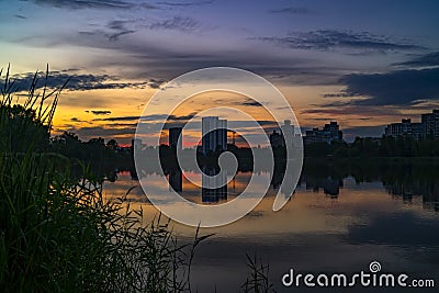 Urban sunset with silhouettes of city buildings on colorful sky and lake background Stock Photo