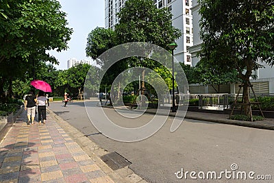Urban walking road among green tree in modern apartment buildings in big city. People walking on the path Editorial Stock Photo