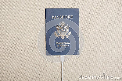 US citizen passport with white cable plugged into the passport on a beige textile backdrop in sunlight Stock Photo