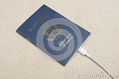 US citizen passport with white cable plugged into the passport on a beige textile backdrop in sunlight Stock Photo