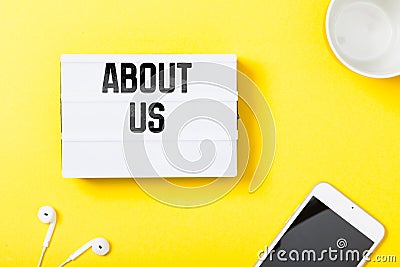 About Us headline in notebook with electronic devces on yellow background Stock Photo