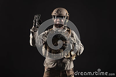 USA soldier in a military suit with a rifle smiles and shows the okay sign against a dark background, an American commando in Stock Photo