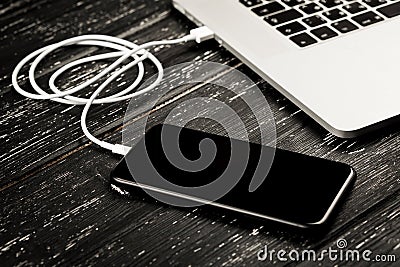 A USB cable connects your phone and laptop. On the black table Stock Photo