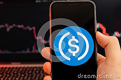 USD Coin USDC cryptocurrency logo on the screen of smartphone in mans hand with downtrend on the chart on a red light Editorial Stock Photo