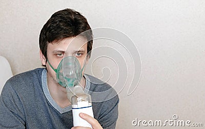 Use nebulizer and inhaler for the treatment. Closeup young man`s face inhaling through inhaler mask. Front view Stock Photo