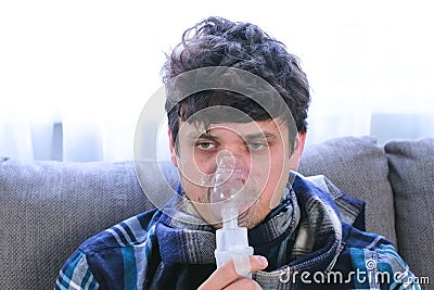 Use nebulizer and inhaler for the treatment. Sick man inhaling through inhaler mask sitting on the sofa. Close-up face. Stock Photo