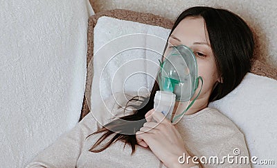 Use nebulizer and inhaler for the treatment. Young woman inhaling through inhaler mask lying on the couch. Closeup front Stock Photo