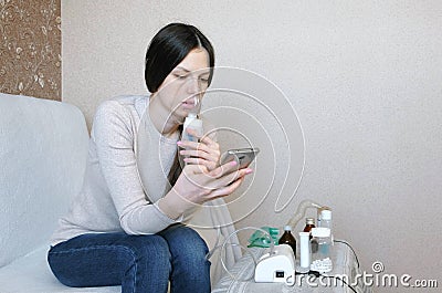 Use nebulizer and inhaler for the treatment. Young woman inhaling through inhaler mask and looking at phone. Side view. Stock Photo