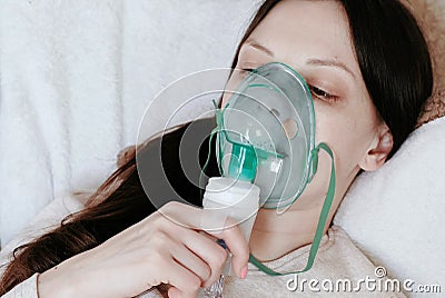 Use nebulizer and inhaler for the treatment. Young woman`s face inhaling through inhaler mask lying on the couch. Side Stock Photo