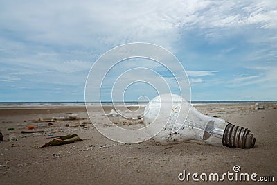 Used light bulb and garbage on the beach Stock Photo