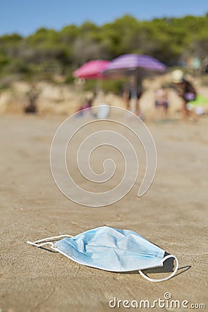 Used surgical mask thrown on the sand of a beach Stock Photo