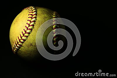 A used yellow softball isolated on a black background. Stock Photo