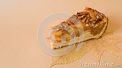 Useful baking. An appetizing piece of apple pie with pecans on autumn leaves on a plain light brown background Stock Photo