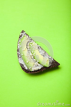 Useful sandwiches with avocado, cheese, sesame and black bread on a bright green background, vertically Stock Photo